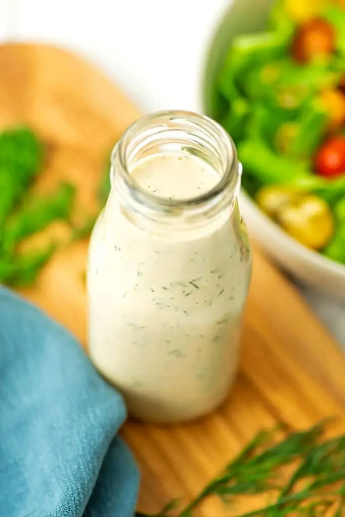 Dill tahini dressing in a dressing bottle sitting on a wooden cutting board.