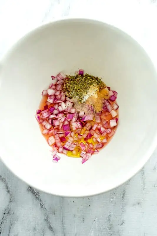 Red onion added to bowl with vinegar and spices.