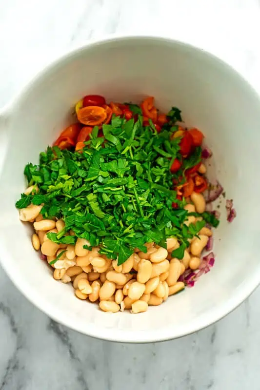 Chopped parsley, white beans and tomatoes in a white bowl. 