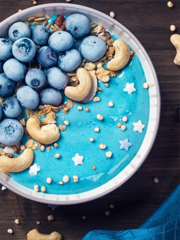 A vibrant protein smoothie bowl with granola, cashews and blueberries on top.