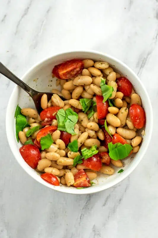 Fresh basil added to white bean and tomato salad in a bowl.