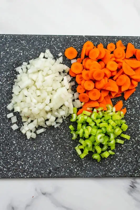 Chopped white onion, celery and carrots on cutting board. 
