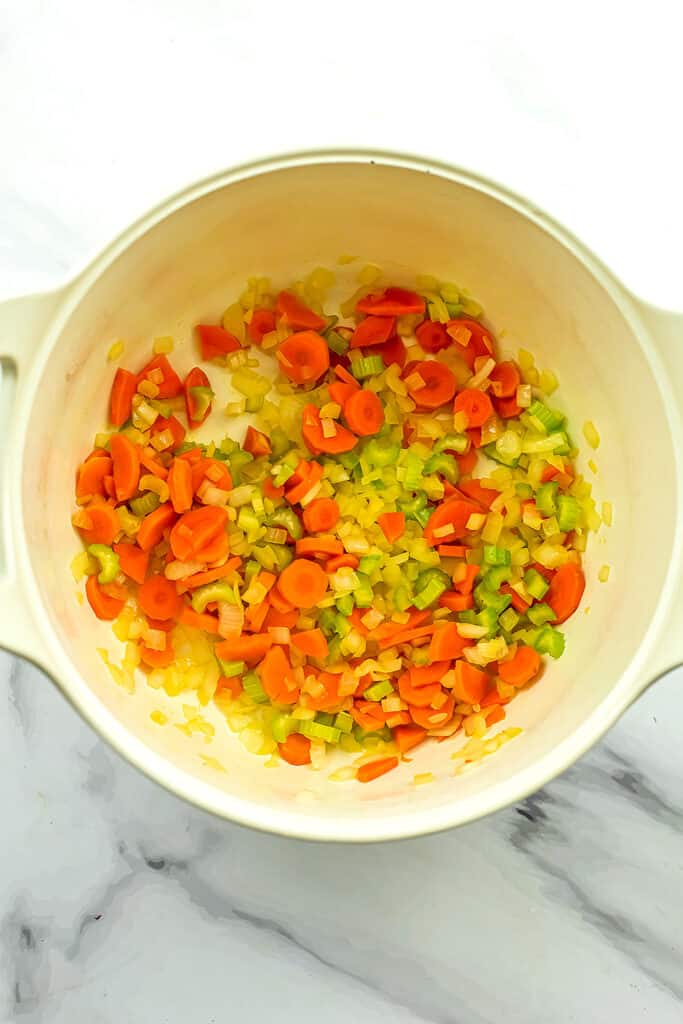 Cooked chopped celery, onion and carrots in large white pot. 