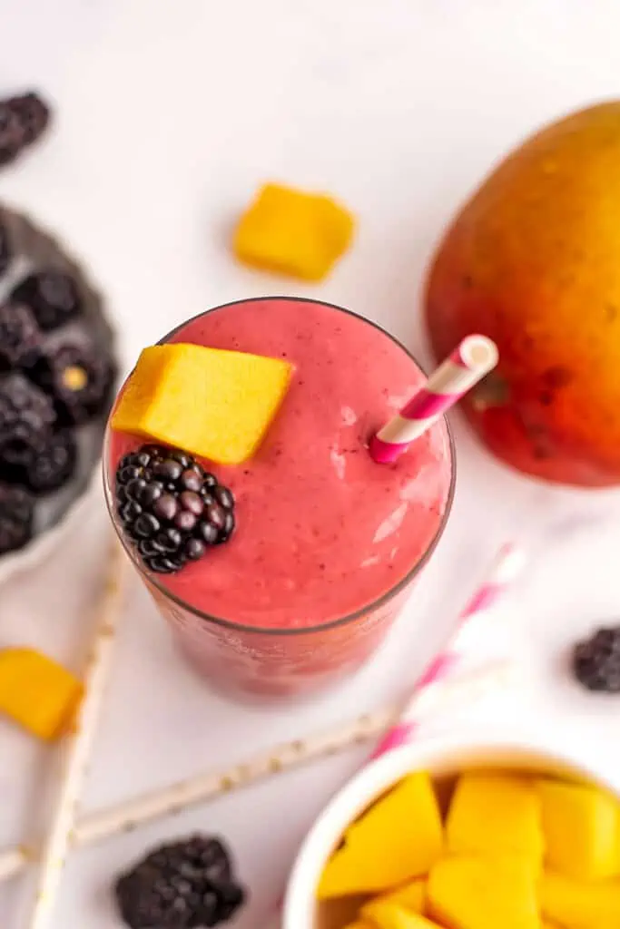 Mango blackberry smoothie with blackberry and mango on top with a straw.