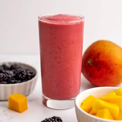 Mango blackberry smoothie in a tall glass on a white table.