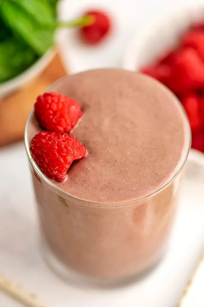 Raspberry smoothie in a glass with raspberries on top.