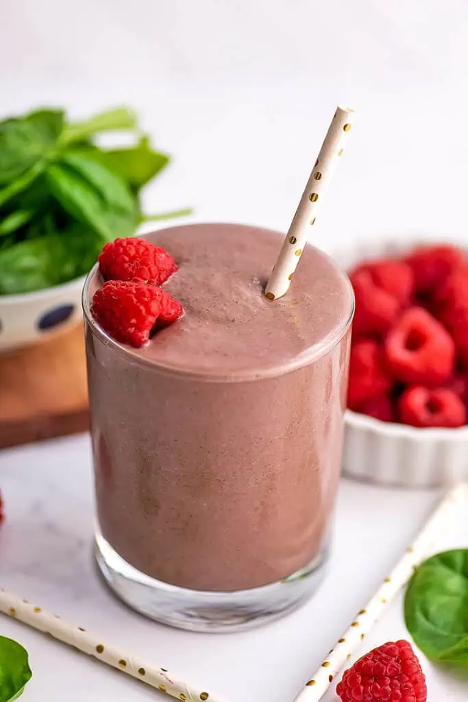 Raspberry spinach smoothie in a small glass with raspberries and a straw on top.