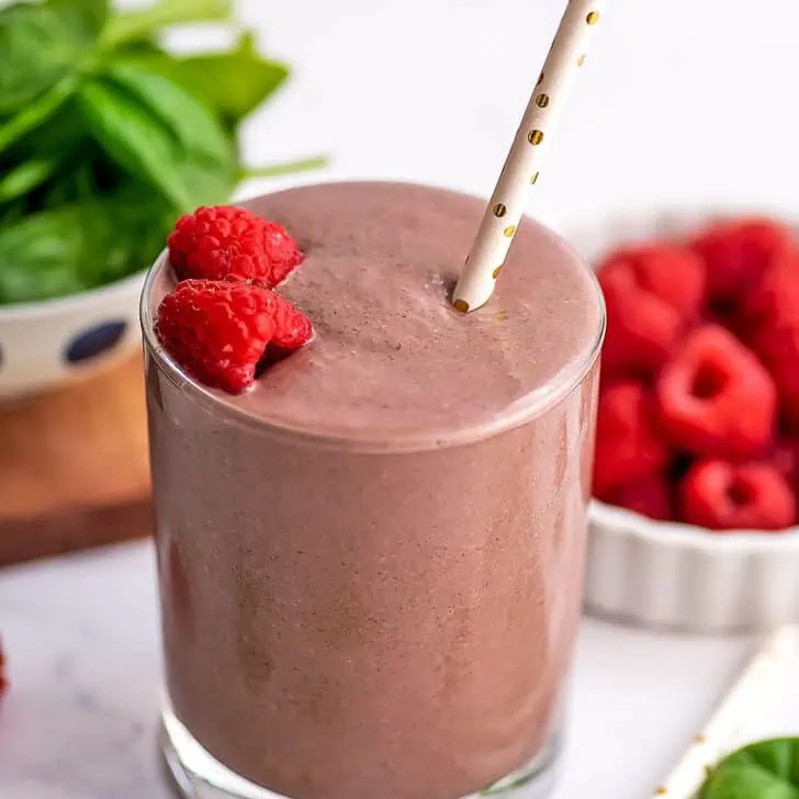 Raspberry spinach smoothie in a small glass with raspberries and a straw on top.