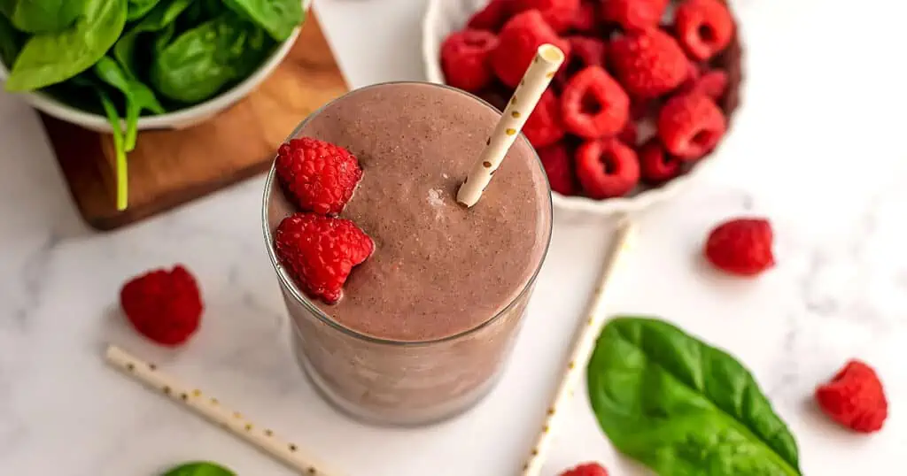 Raspberry spinach smoothie with raspberries and a straw on top.