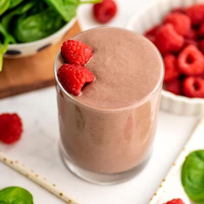 Raspberry green smoothie in a small glass with two raspberries on top.