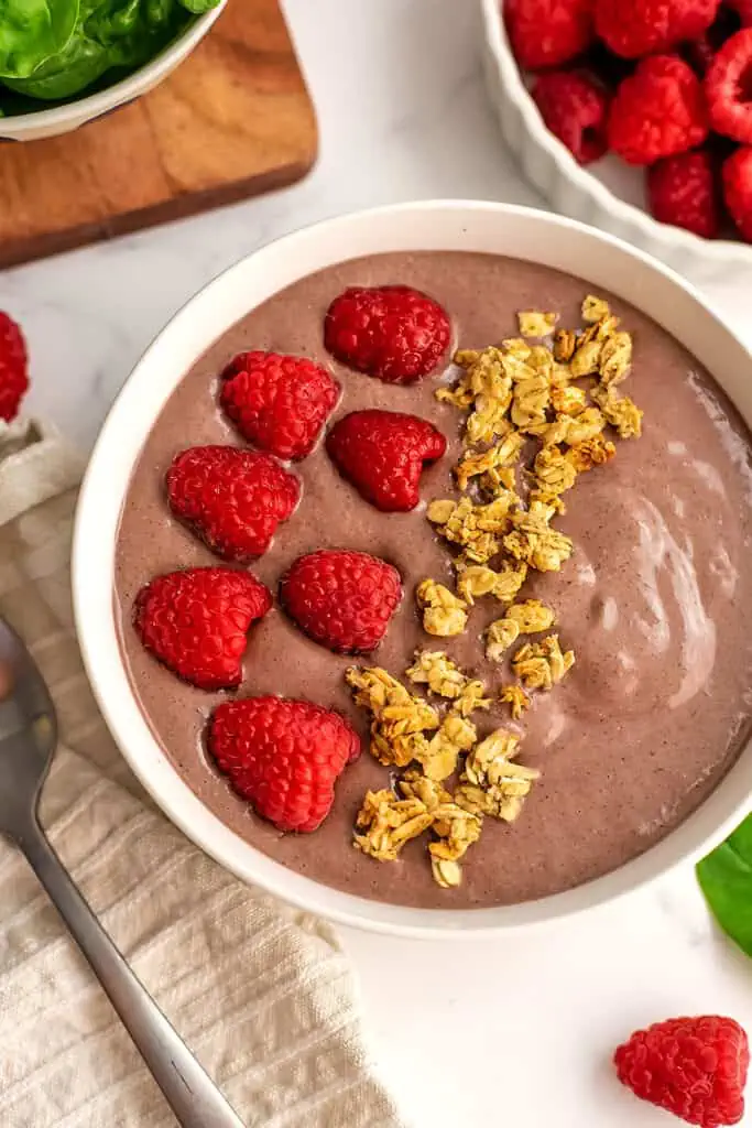 Spinach raspberry smoothie bowl with granola and raspberries on top.