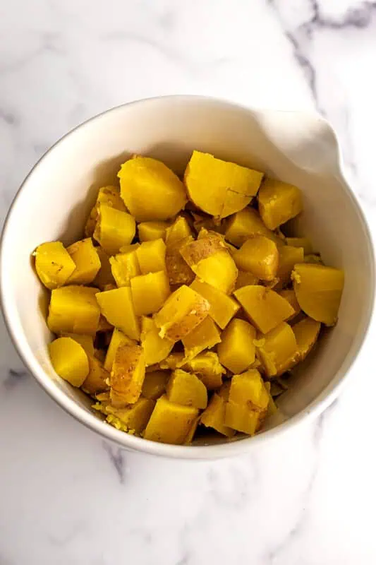 Cooked potatoes cut into cubes in a large white bowl.