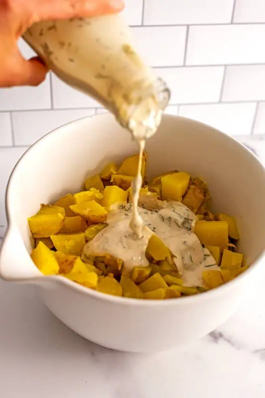 Dill dressing being poured over potatoes in a bowl.