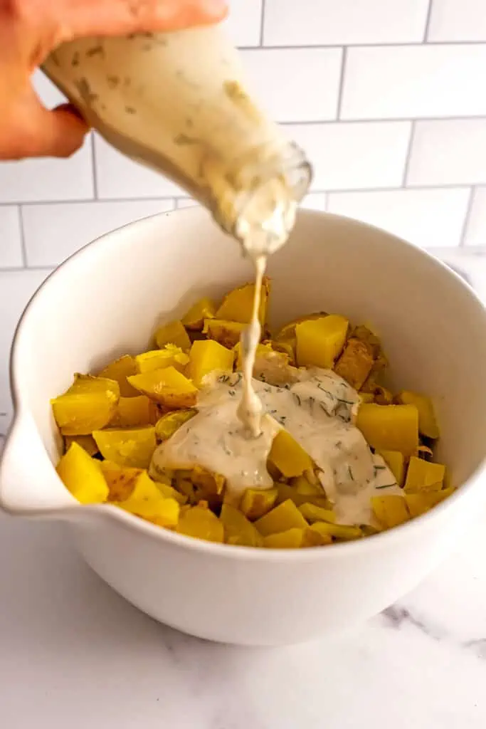 Potatoes with dill tahini dressing being poured on them in a large white bowl.