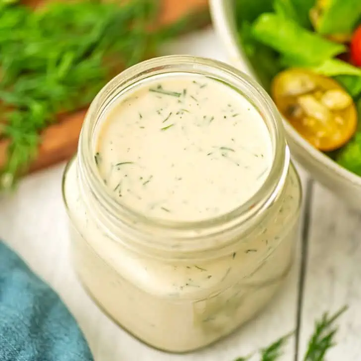 Vegan dill dressing in a small bottle on a white table.