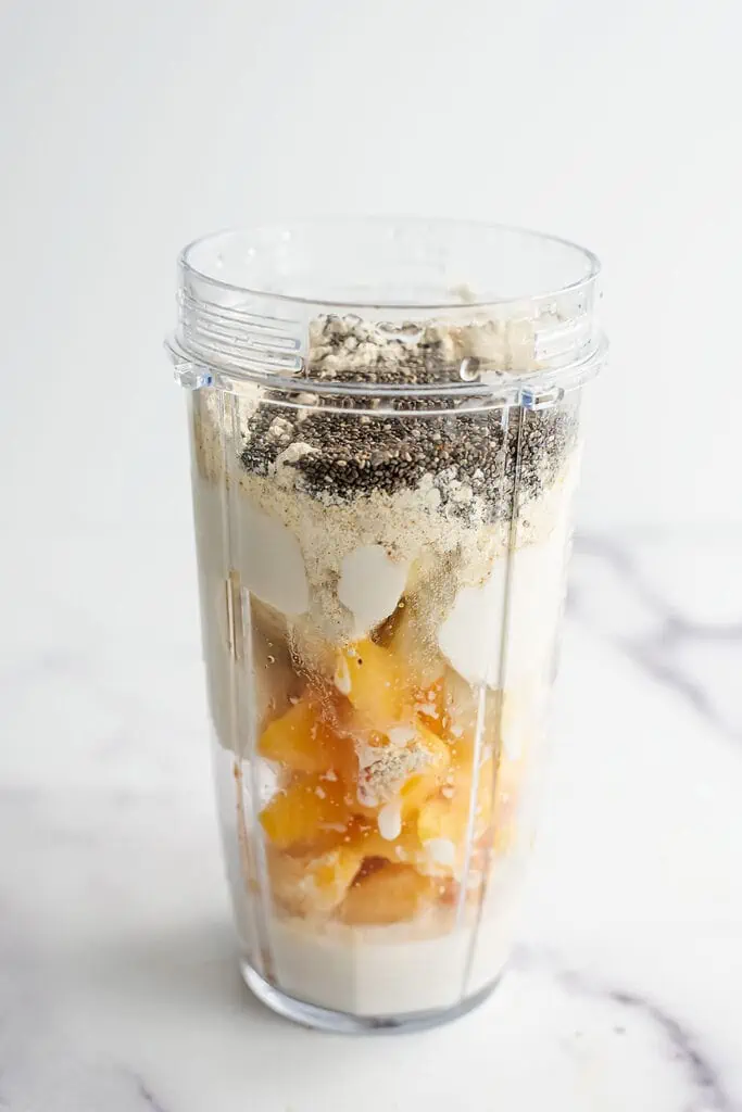 Banana peach smoothie bowl in a blender cup before being blended.