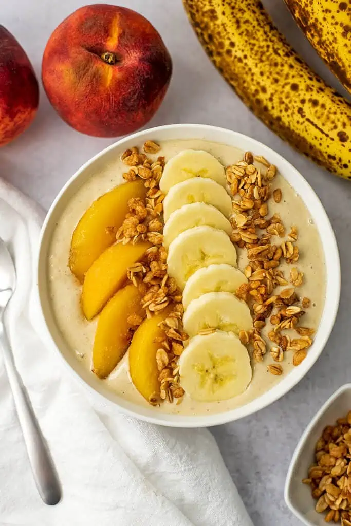 Banana peach smoothie bowl recipe with sliced peaches, banana and granola on top.