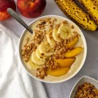Banana peach smoothie in a bowl with sliced banana, peaches and granola.