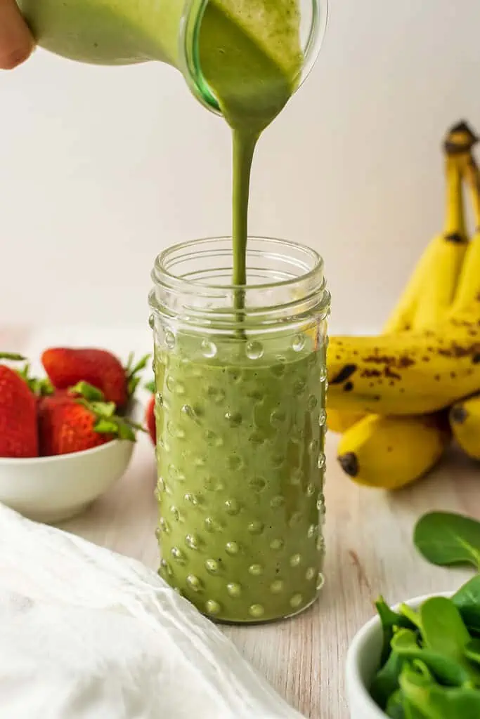 Banana strawberry spinach smoothie being poured into a large glass.