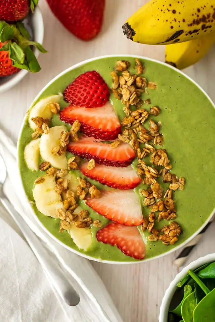 Banana strawberry spinach smoothie in a bowl with sliced strawberries, banana and granola on top.