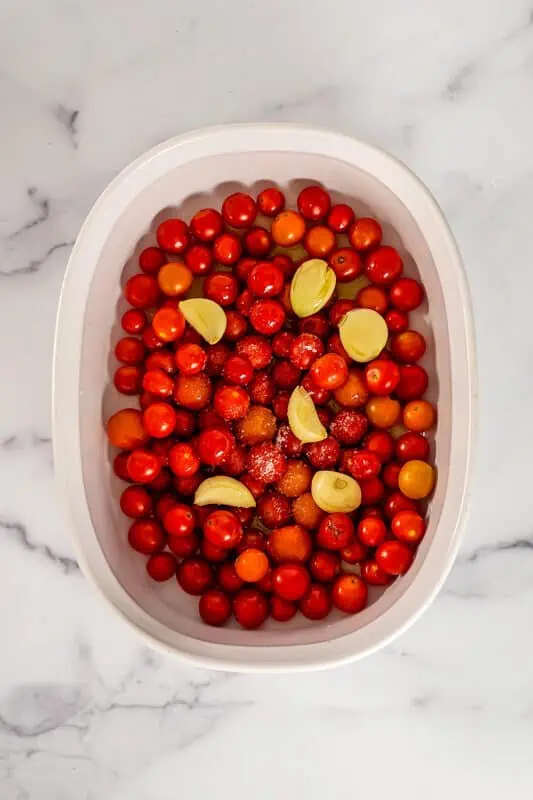 Casserole dish filled with cherry tomatoes, garlic and olive oil.