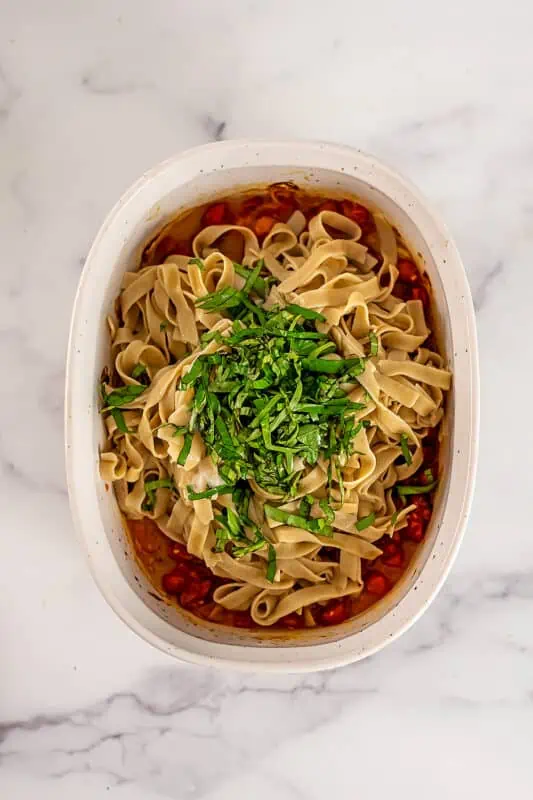 Fresh basil, pasta and cherry tomato pasta cause in a large casserole dish.