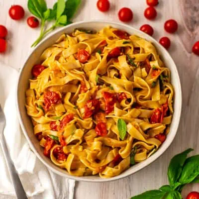 Cherry tomato pasta sauce served in a white bowl with scattered cherry tomatoes around it on a white table.