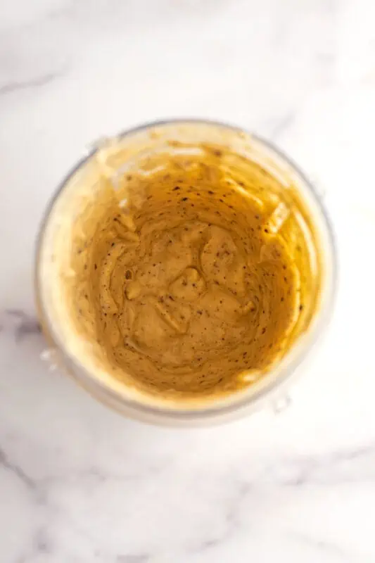 Cookie dough smoothie bowl in a blender cup after 3 pulses with cacao nibs.