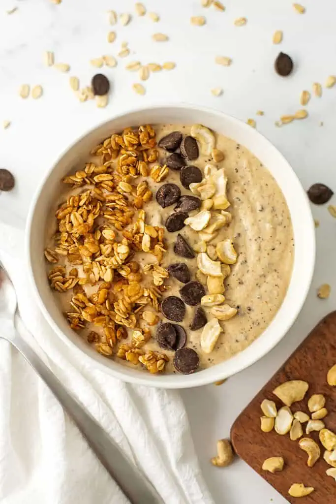 Cookie dough smoothie bowl with granola, cashews, and chocolate chips on a white table.