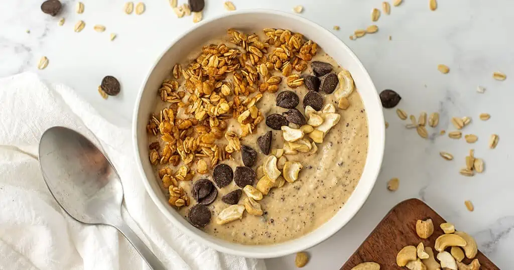 Cookie dough smoothie bowl with granola, chocolate and nuts on top.