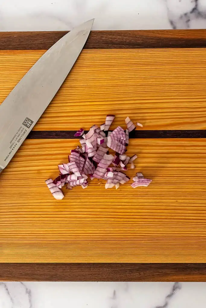 Red onion finely chopped on wood cutting board with knife on board. 