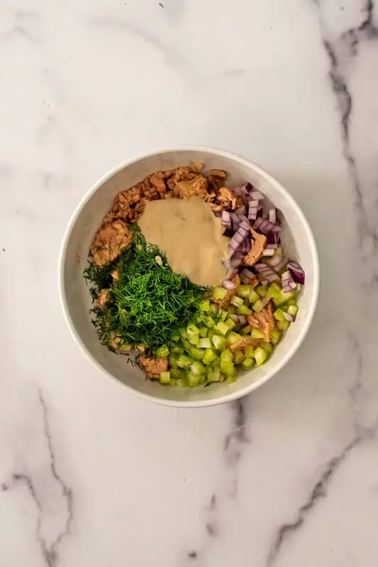 Chopped veggies, tuna and tahini dressing in bowl.
