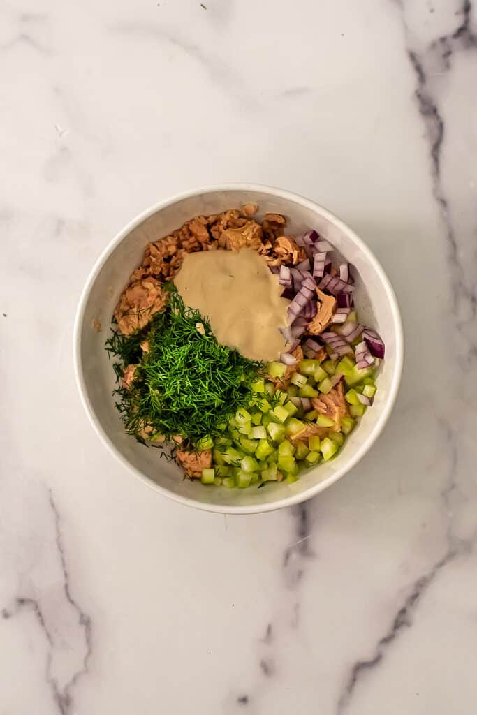 Chopped veggies, tuna and tahini dressing in bowl.