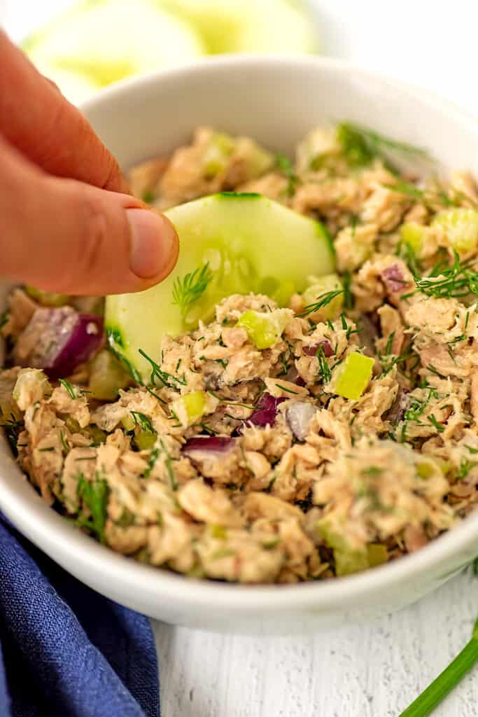 Dill tuna salad being used as a dip with a piece of cucumber.