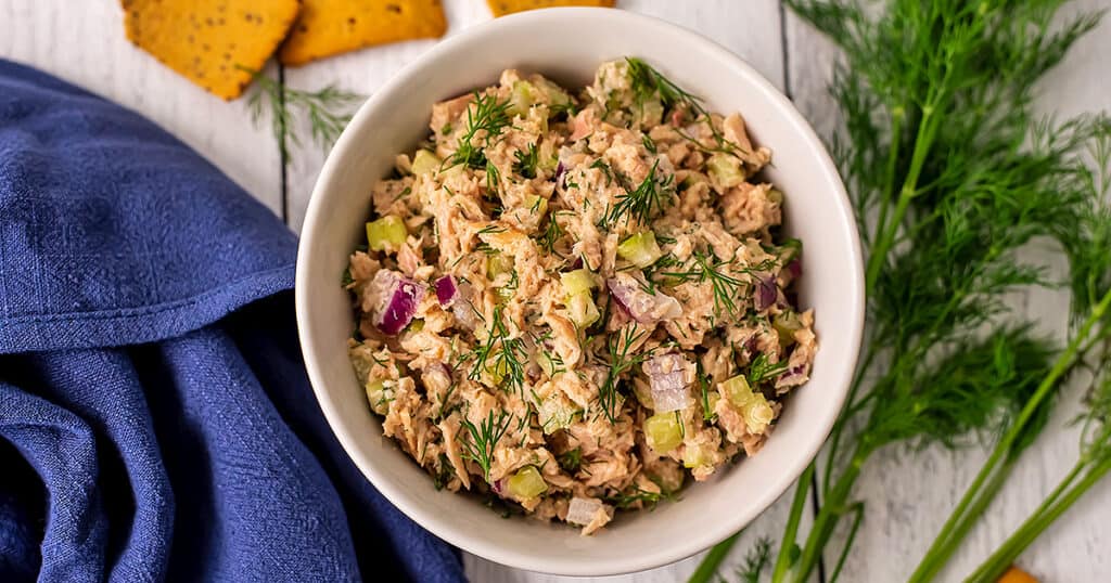 Dill tuna salad on a white table with crackers and fresh dill.