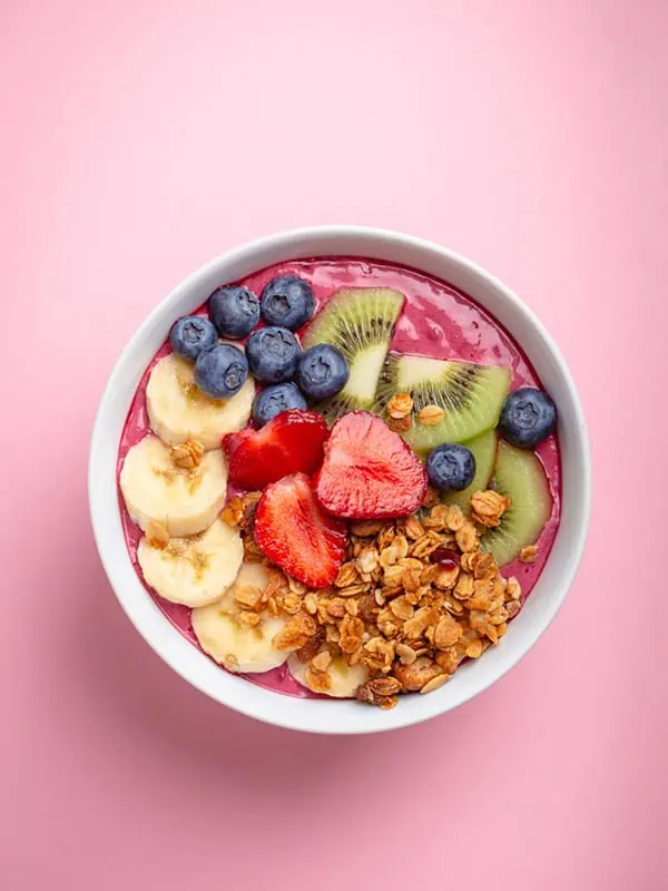 A delicious smoothie bowl with loads of toppings including banana, strawberry, blueberry, granola and kiwi.