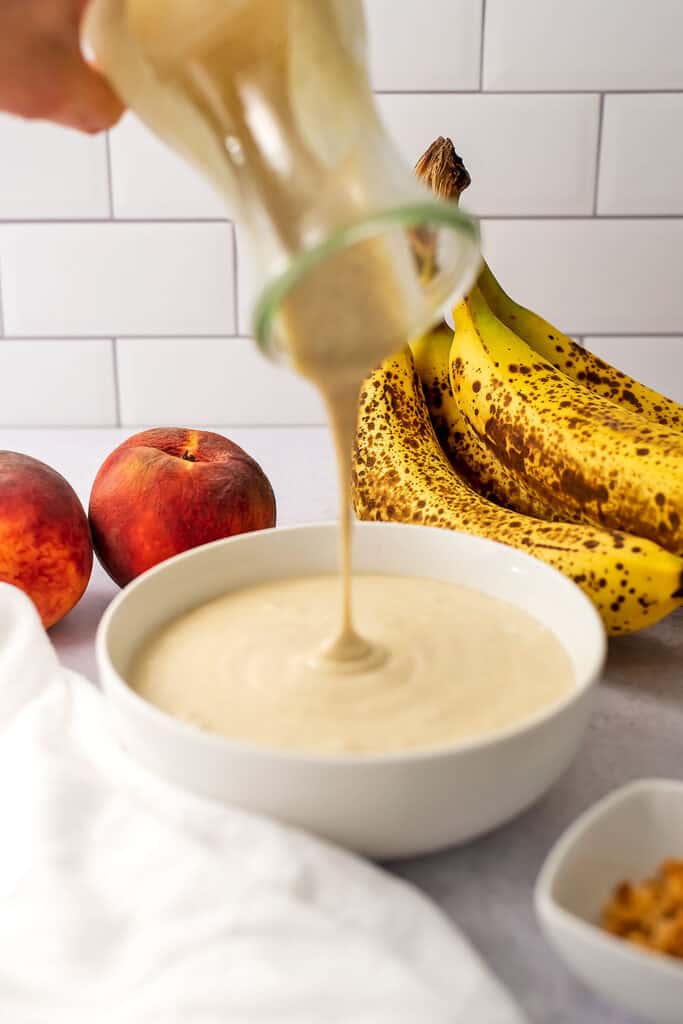 Peach and banana smoothie bowl being poured into a bowl. 