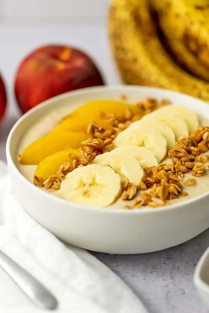 Peach banana smoothie bowl with granola, fresh peaches and cut up bananas on top.