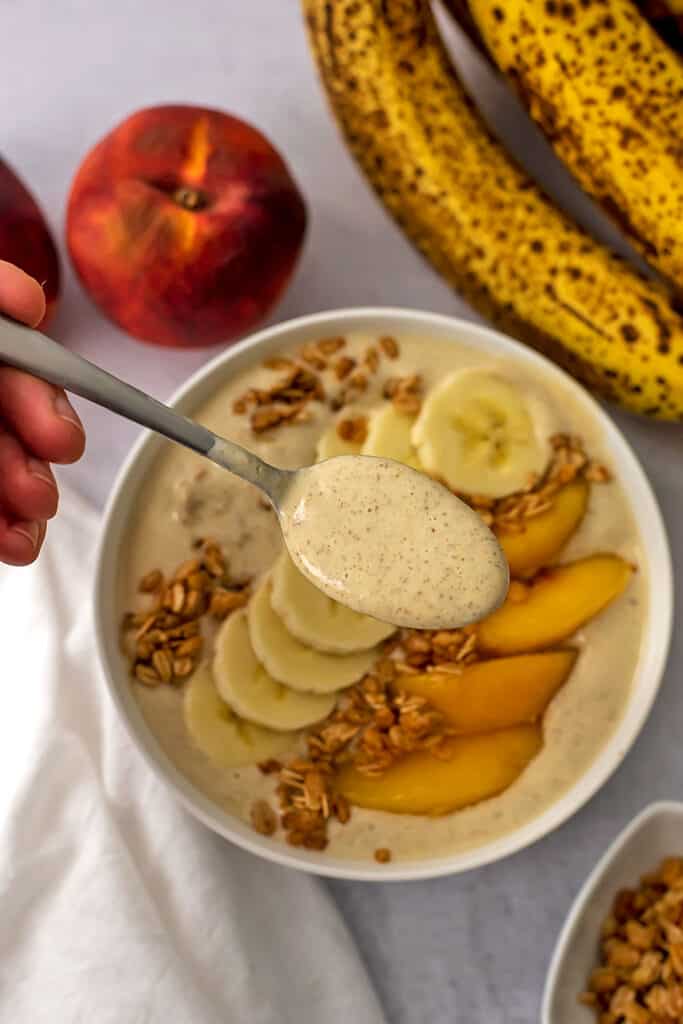 Peach banana smoothie bowl with sliced bananas, peaches and granola on top.