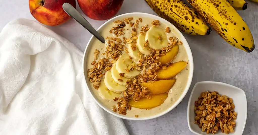Peach banana smoothie bowl with sliced bananas, peaches and granola on top.