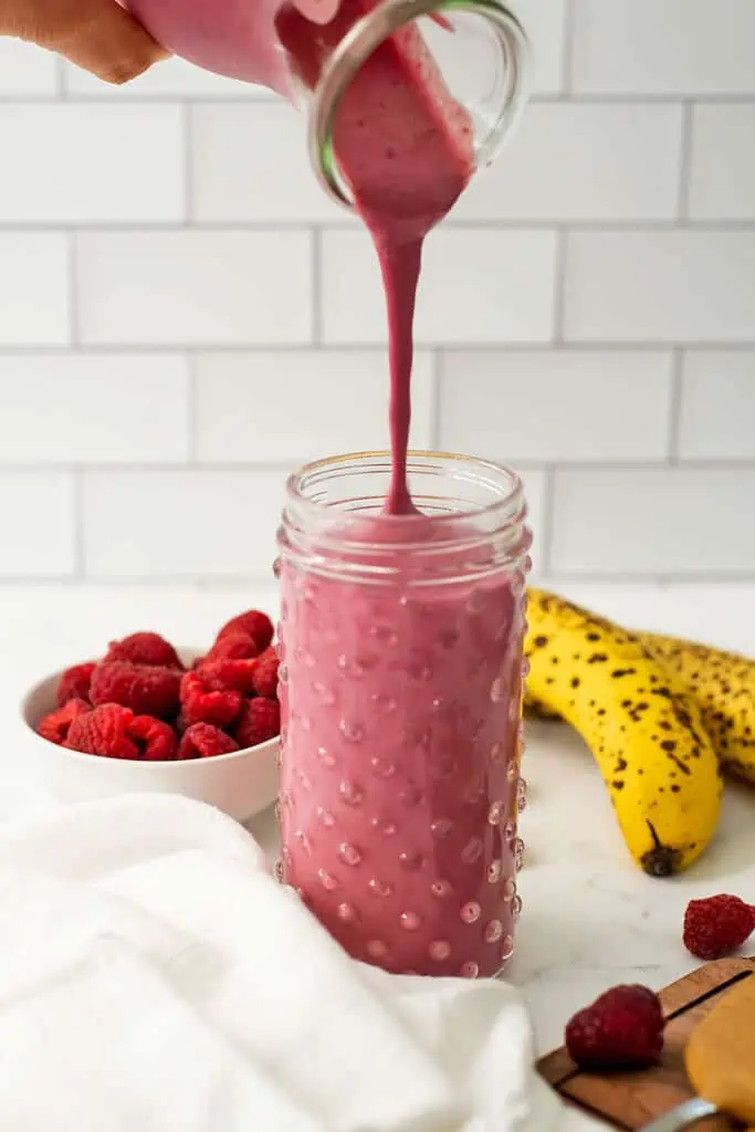 Peanut butter raspberry smoothie being poured into a glass.