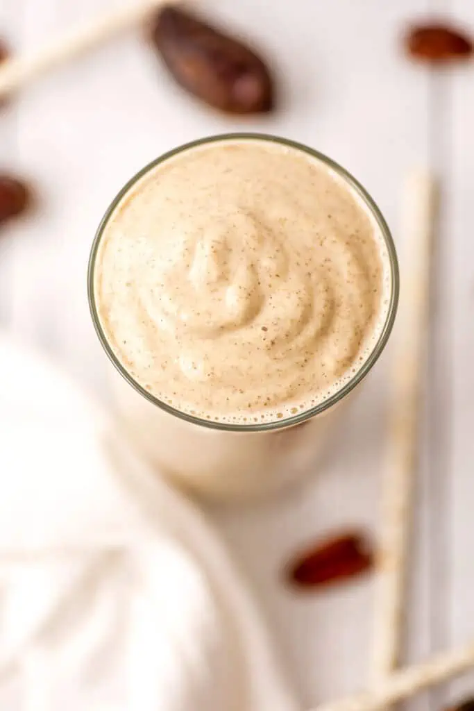 Overhead view of a pecan smoothie in a glass on a white surface. 