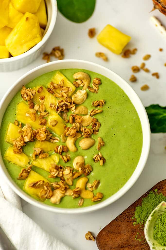 Pineapple matcha smoothie in a smoothie bowl with granola and pineapple slices on top.