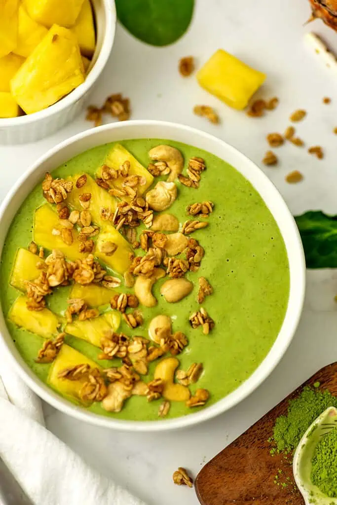 Pineapple matcha smoothie in a smoothie bowl with granola and pineapple slices on top.