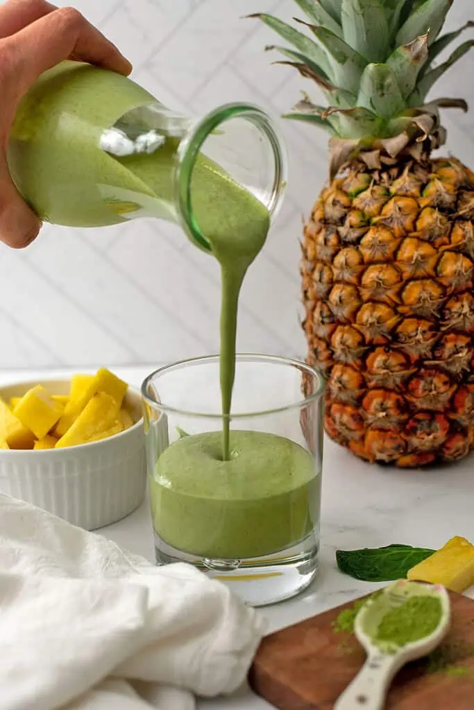 Pineapple matcha smoothie being poured into a glass.