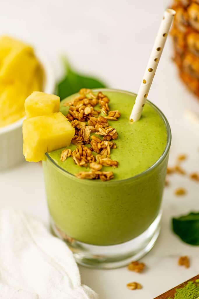 Pineapple matcha smoothie in a short glass with pineapple chunk and granola on top.