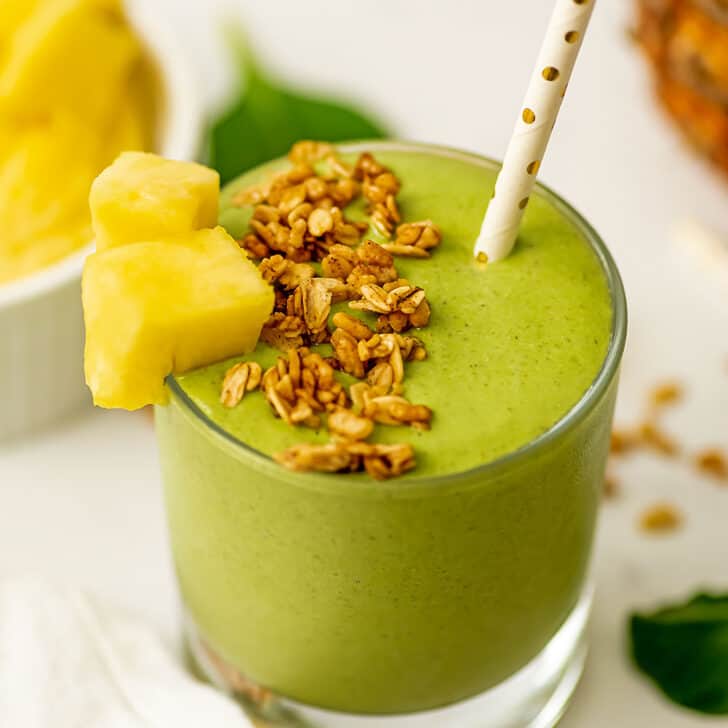 Pineapple matcha smoothie in a short glass with pineapple chunk and granola on top.