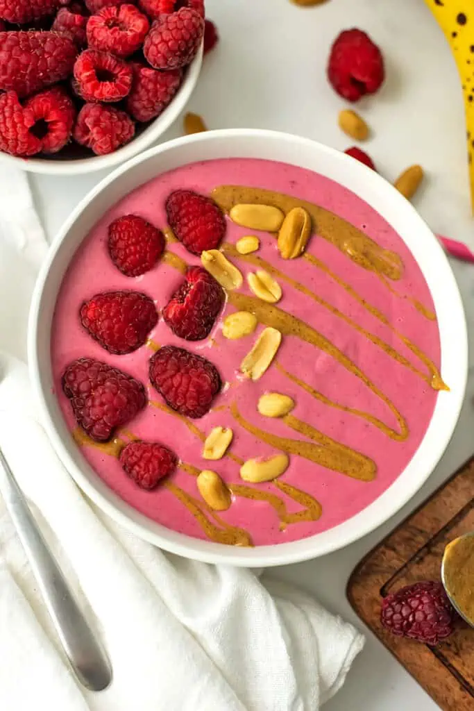 Raspberry peanut butter smoothie in a bowl with peanuts, peanut butter drizzle and raspberries on top.