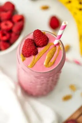 Raspberry peanut butter smoothie with raspberries and peanut butter drizzle on top with a straw.