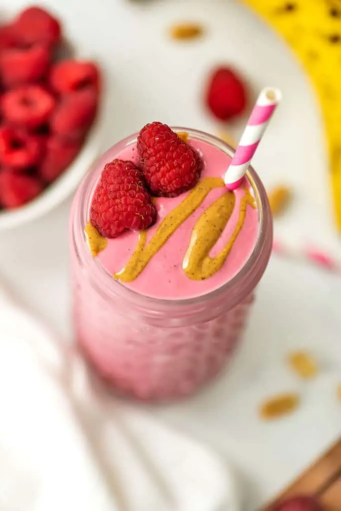 Raspberry peanut butter smoothie with raspberries and peanut butter drizzle on top with a straw.